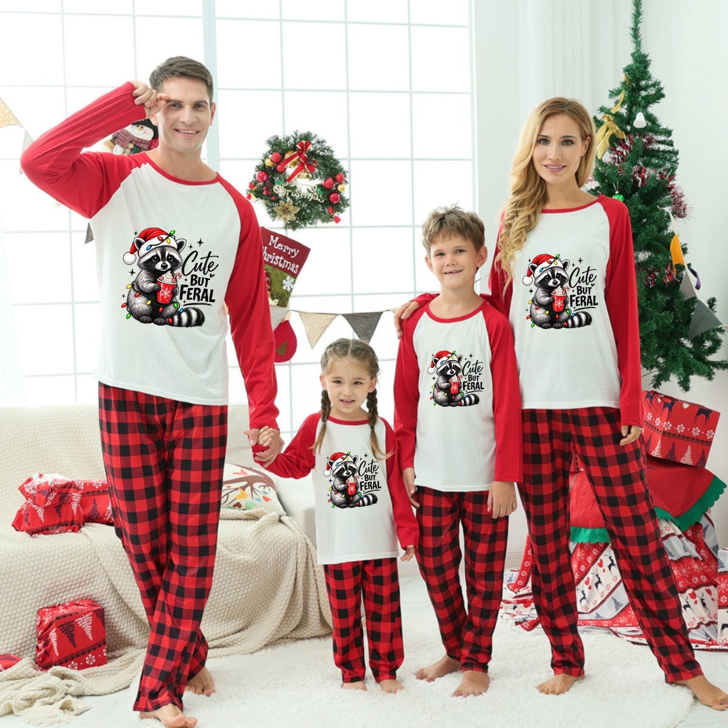 A family of four wearing matching Christmas-themed long-sleeve pajamas stands together in a decorated living room. The pajamas have red and black buffalo plaid legs with white fronts and red sleeves, featuring a festive Santa graphic.