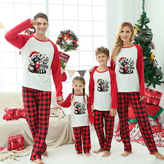 A family of four wearing matching Christmas-themed long-sleeve pajamas stands together in a decorated living room. The pajamas have red and black buffalo plaid legs with white fronts and red sleeves, featuring a festive Santa graphic.
