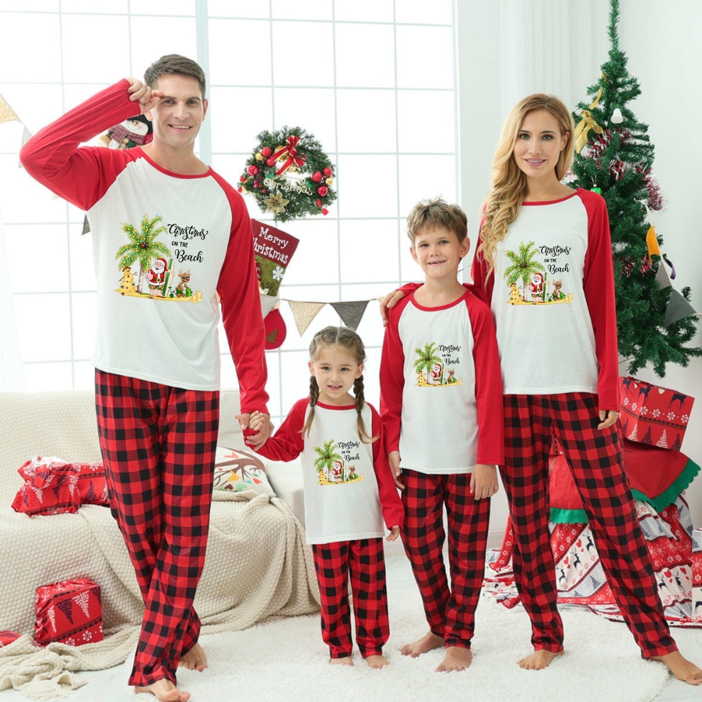 A family of four wearing matching Christmas-themed long-sleeve pajamas with Red and Black buffalo plaid pants, standing in a decorated living room with a Christmas tree and wrapped gifts.