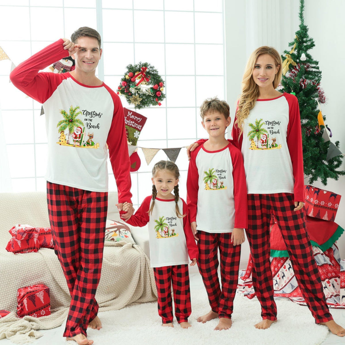 A family of four wearing matching Christmas-themed long-sleeve pajamas with Red and Black buffalo plaid pants, standing in a decorated living room with a Christmas tree and wrapped gifts.