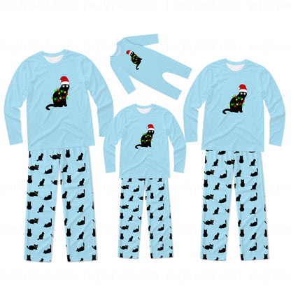 Three sizes of matching family pajama sets shown on a white background. Each set includes a light blue long-sleeve top with a black cat wearing a Christmas tree and Santa hat graphic, paired with light blue pants covered in a black cat print.