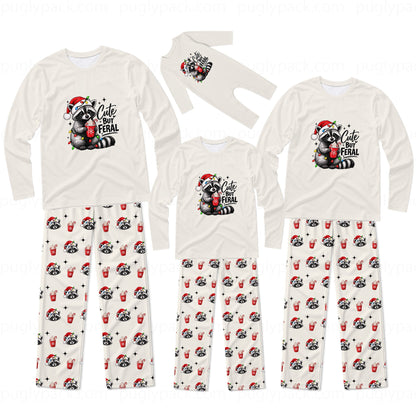 A matching family Christmas pajama set with long-sleeve shirts and pants in cream white. The shirts feature a cute raccoon wearing a Santa hat and holding a red mug with the text 'Cute But FERAL'.