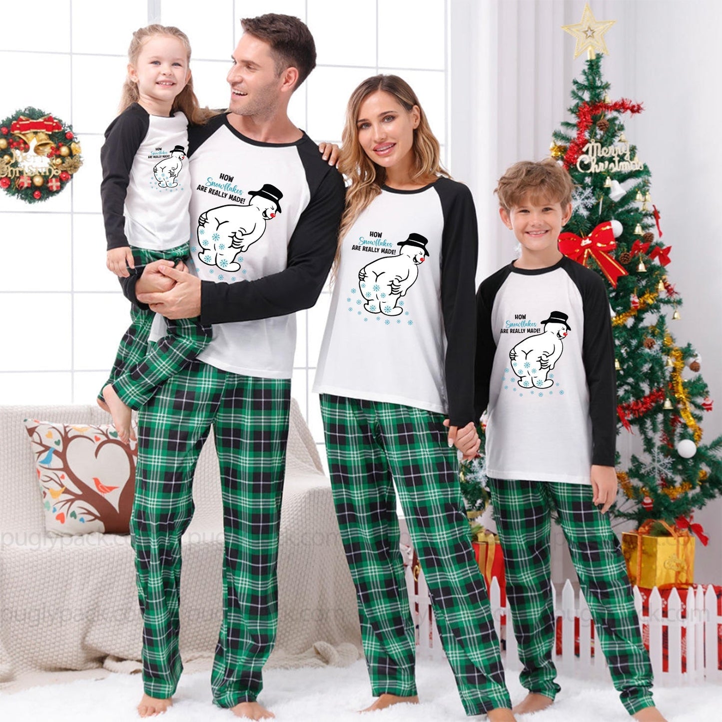 A family of four wearing matching Christmas pajamas, including a dad, mom, and two children, standing together in a festive living room with a decorated Christmas tree and wreath.