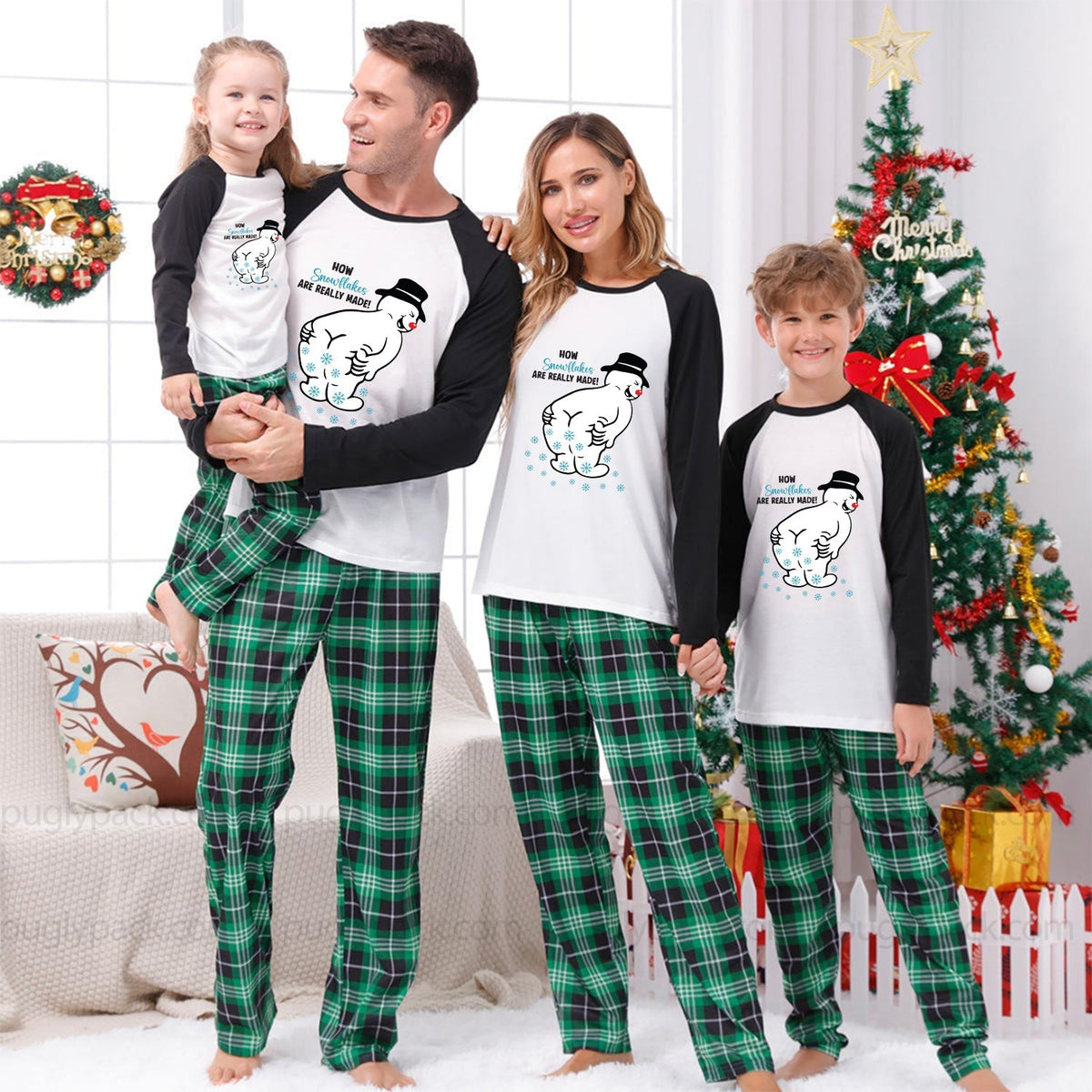 A family of four wearing matching Christmas pajamas, including a dad, mom, and two children, standing together in a festive living room with a decorated Christmas tree and wreath.