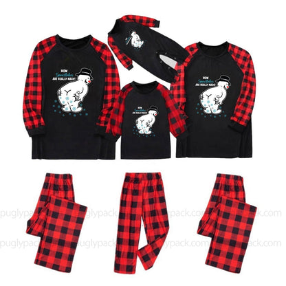 Three matching family Christmas pajama sets shown on a White background, including long-sleeve shirts and pants. The shirts are Black with Red buffalo plaid sleeves and a White cartoon snowman graphic with the text 'HOW'S EVERYTHING?' and 'DO WE HAVE TO WAIT?'.