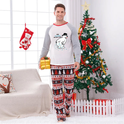 A man modeling a two-piece Christmas pajama set in a decorated living room with a Christmas tree, stocking, and couch. The pajama set features a White long-sleeve top with Red trim and a cartoon polar bear graphic, paiRed with matching Red, White, and Blue patterned pants.