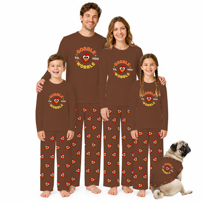 A family of four wearing matching brown long-sleeve pajamas with a 'COBBLE THE WOBBLE' graphic and Red-and-yellow heart pattern, standing on a White background with a small dog at the bottom right.