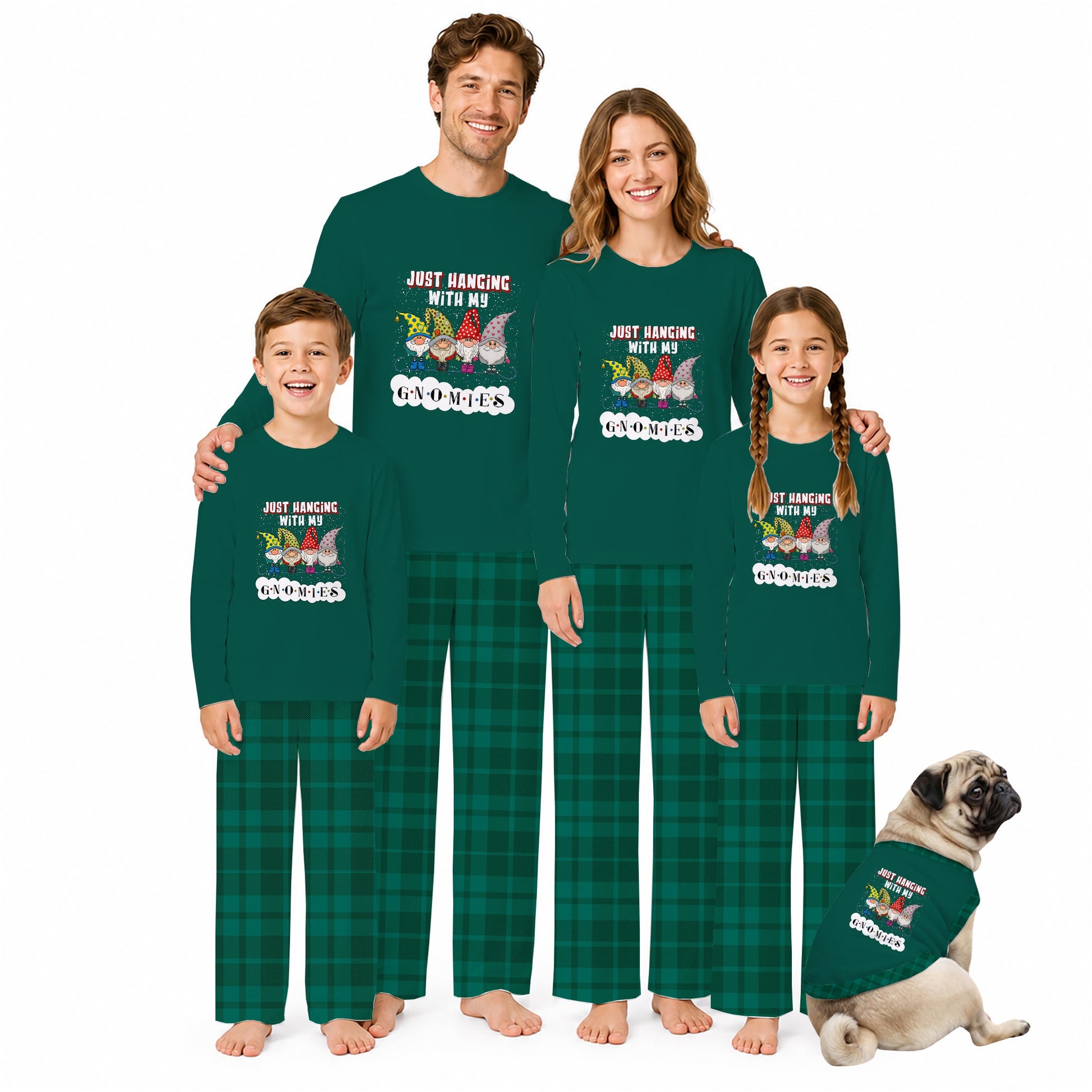 A family of four wearing matching dark Green long-sleeve pajamas with a gnome graphic and the text 'JUST HANGING WITH MY Gnomes' stands barefoot against a White background, with a small pug dog wearing a matching pajama set beside them.