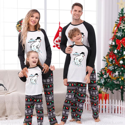 A family of four wearing matching Christmas pajamas stands together in a living room setting with a decorated Christmas tree, couch, and holiday decorations. The pajamas feature a White front with Black long sleeves and a cartoon snowman graphic, paiRed with Black and White patterned pants.