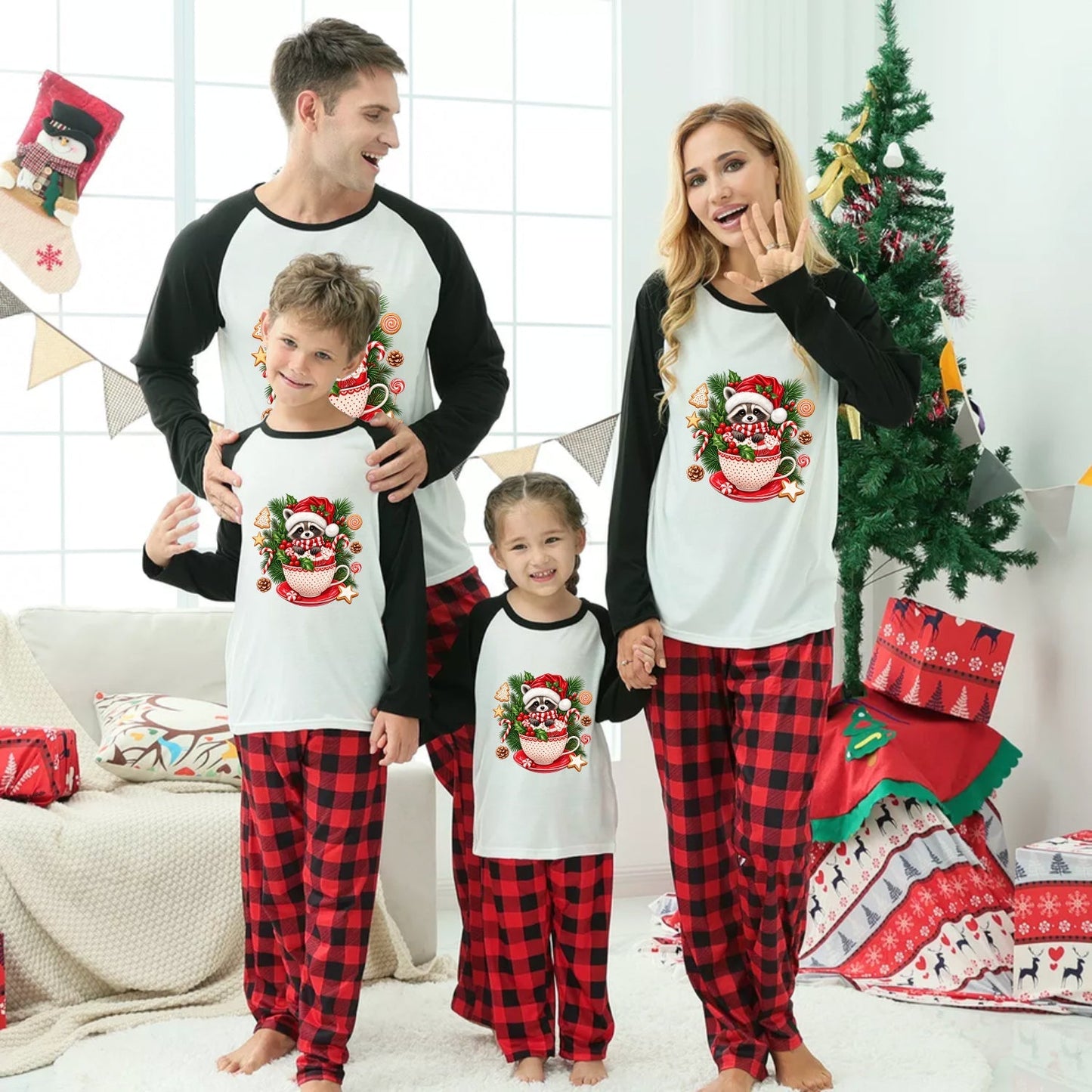 A family of four wearing matching Christmas pajamas stands in a decorated living room with a Christmas tree, gifts, and a couch. The pajamas feature a white torso with black sleeves and a red-and-black buffalo plaid lower body, with a festive Raccoon graphic on the chest.