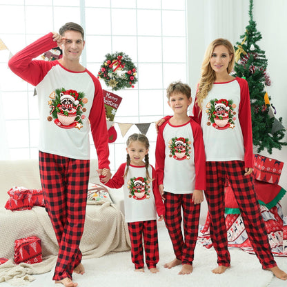A family of four wearing matching Christmas-themed long-sleeve pajamas stands together in a decorated living room. The pajamas have red and black buffalo plaid legs with white fronts and red sleeves, featuring a festive Raccoon graphic.
