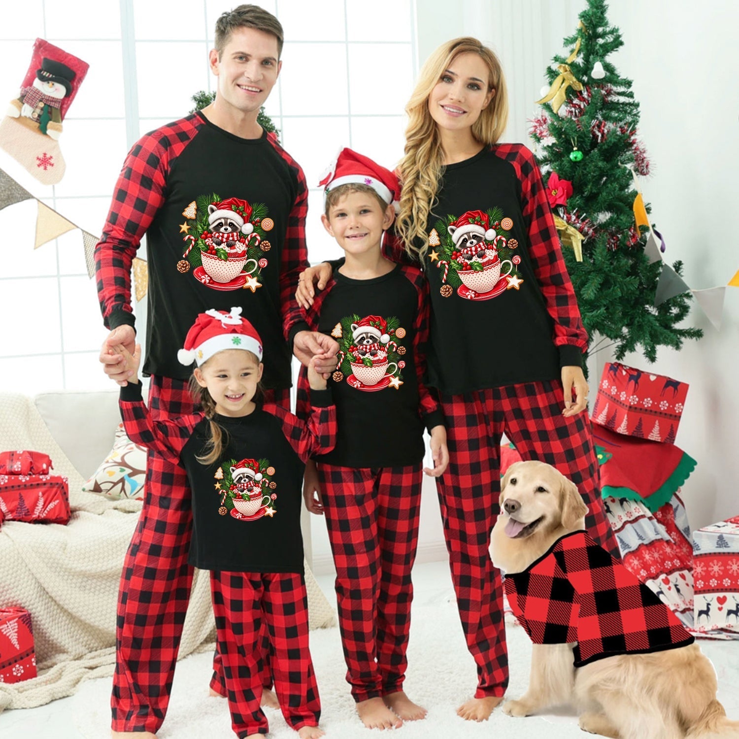 A family of four wearing matching black and red Christmas pajamas with a Santa cup graphic, standing in a decorated living room with a dog wearing a matching red and black sweater.